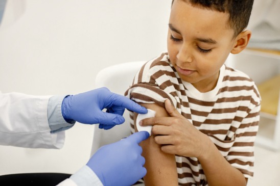 Male doctor holding a cotton on a shoulder. Man wearing white medical gown. Boy wearing brown plaid t-shirt.
