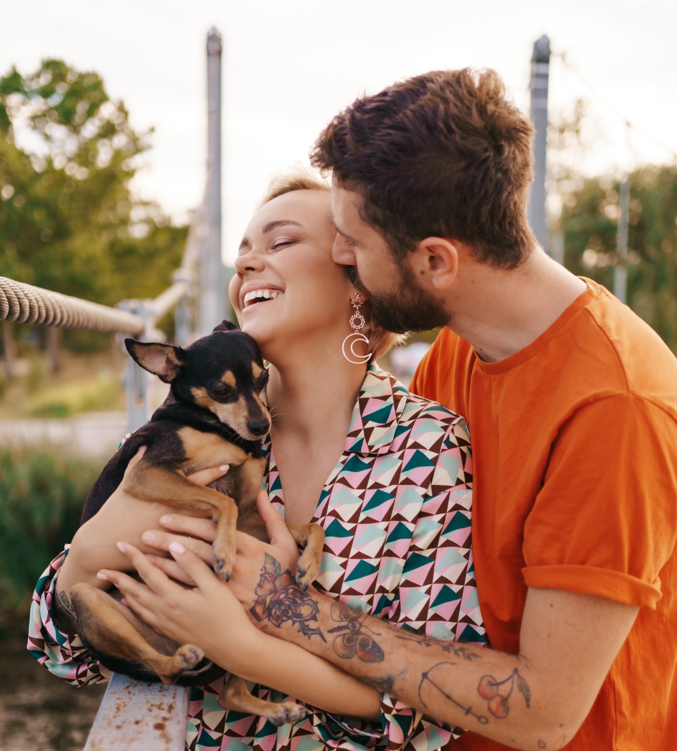 Happy smiling young couple hugging their dog on bridge