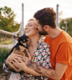 Happy smiling young couple hugging their dog on bridge