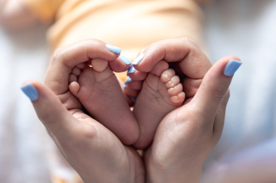 Mom holds the legs of a newborn baby in her hands, close-up, soft focus, concept of motherhood and care.