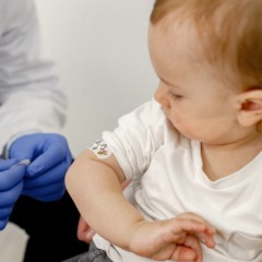 Cropped photo of a little boy in hospital. Medical worker wearing blue gloves and face mask. Boy wearing white t-shirt.