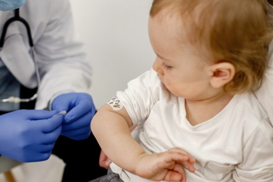 Cropped photo of a little boy in hospital. Medical worker wearing blue gloves and face mask. Boy wearing white t-shirt.